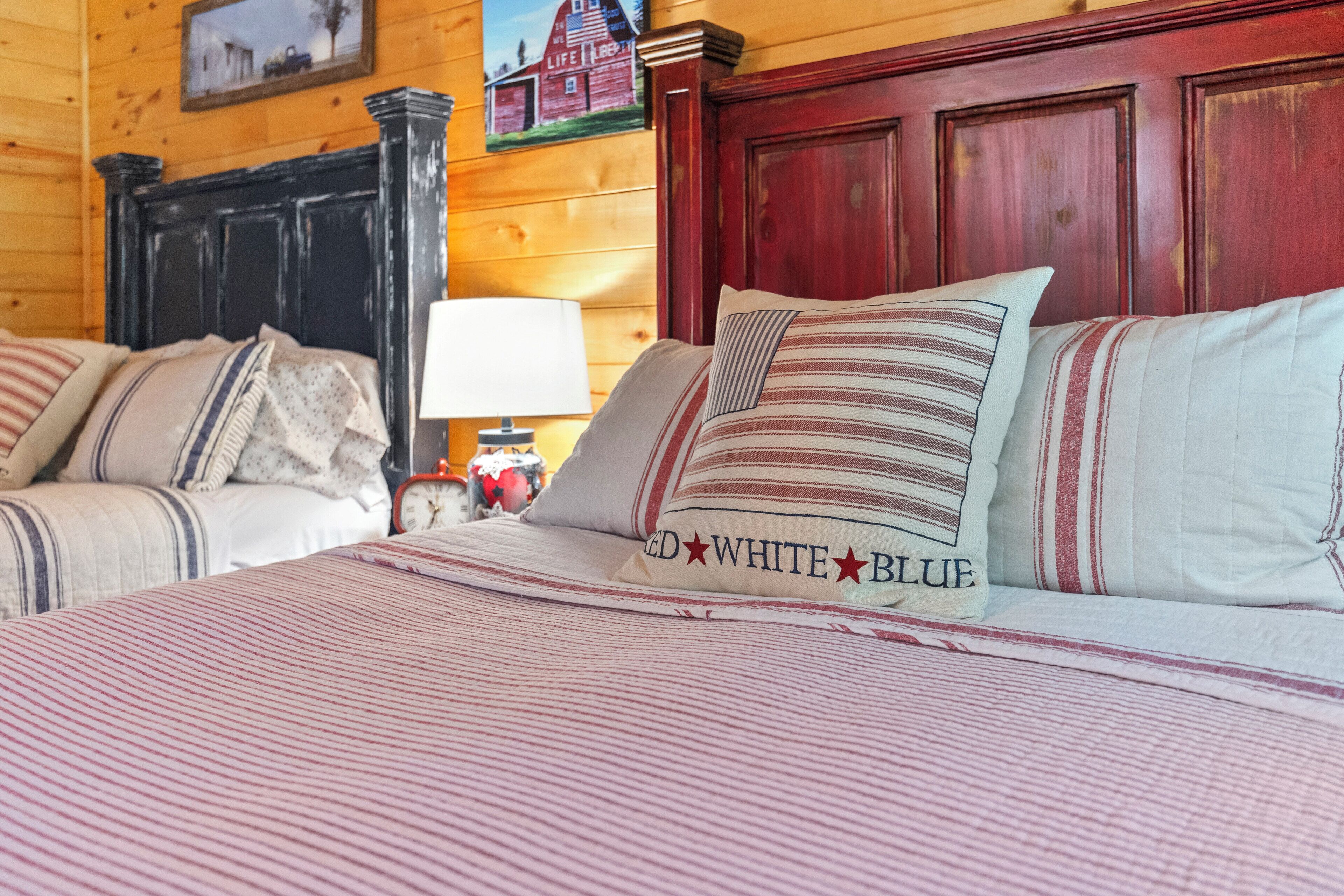 Uma cama com roupa de cama e almofadas listradas, cabeceira de madeira, mesa de cabeceira com abajur e um quadro na parede.