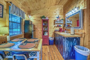 A cabin interior with a dining table, chairs, a refrigerator, a sink, and a mirror.