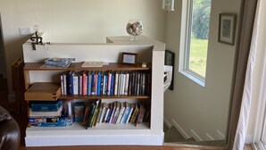 A cozy reading nook with a bookshelf, a lamp, and a window with a view of greenery.