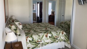 A bedroom with a bed, a ceiling fan, a TV mounted on the wall, and a door leading to another room.