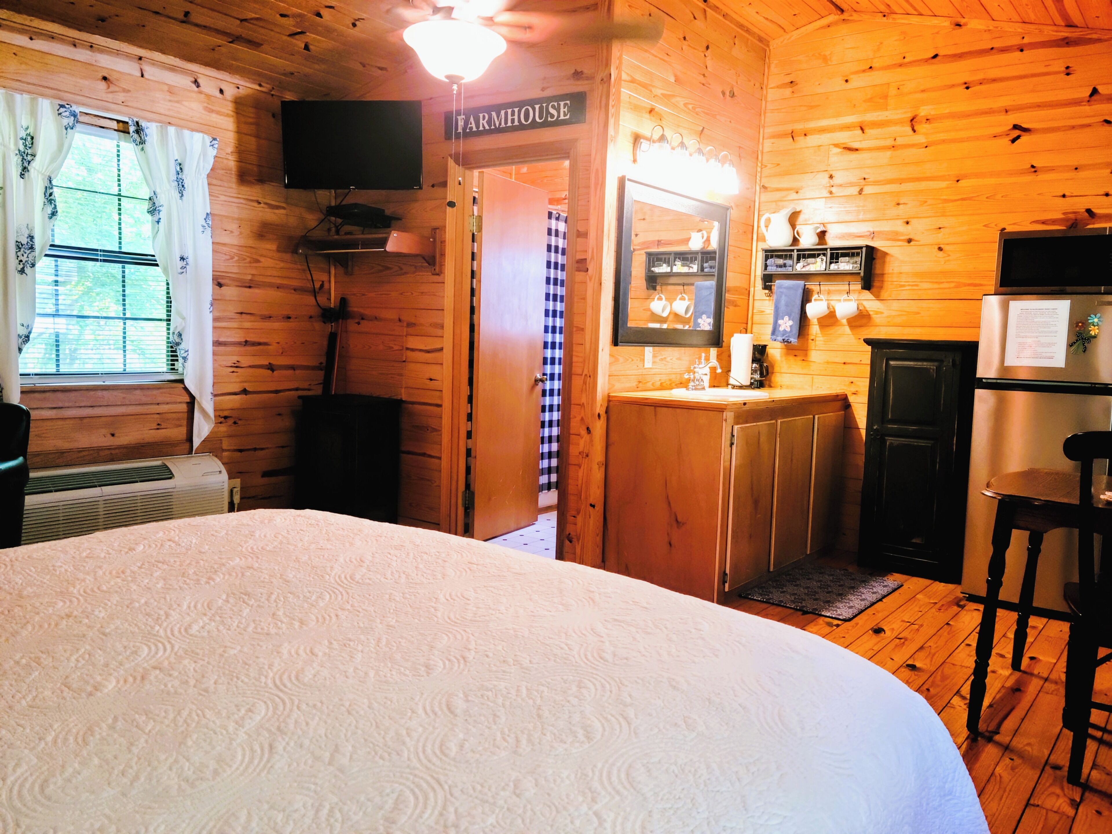 Una habitación de cabaña de madera con una cama, un televisor, una cocina y un letrero que dice 'FARMHOUSE'.