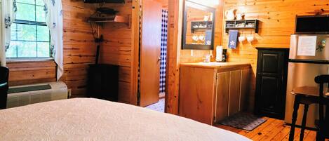 Una habitación de cabaña de madera con una cama, un televisor, una cocina y un letrero que dice 'FARMHOUSE'.