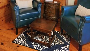 Una habitación acogedora con paredes de madera, una chimenea, dos sillones azules, una mesita de madera y una alfombra estampada.