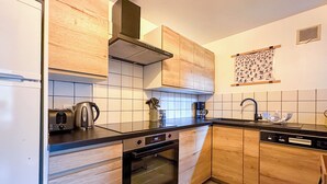 A modern kitchen with wooden cabinets, a black countertop, a built-in oven, a coffee maker, and a kettle. - Charming 3 Bedroom Alpine Apartment. Central location and with beautiful views (Samoëns)