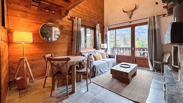 A cozy log cabin interior with a dining area, a sofa, and a fireplace. - Charming 3 Bedroom Alpine Apartment. Central location and with beautiful views (Samoëns)