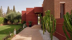 A modern building with a red facade, a paved walkway, and cacti in the garden.