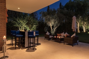 Uma área de pátio externa com mesa de jantar, banquetas de bar e um conjunto de sofás.