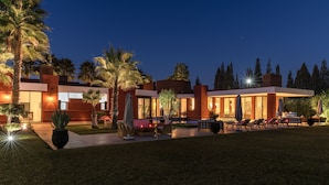 A modern house with a swimming pool, outdoor seating, and palm trees.
