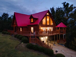Une cabane en rondins avec un toit rouge, une terrasse couverte et des fondations en pierre.