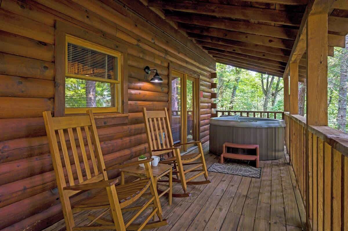 Une cabane en bois avec une véranda, des fauteuils à bascule, une table et un jacuzzi.