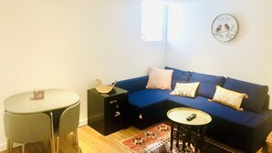 Un salon avec un canapé bleu, une petite table ronde, une chaise, un meuble et une horloge murale.