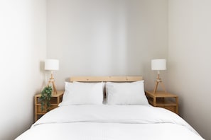 A neatly made bed with white linens, two bedside tables with lamps, and a small plant on one of the tables. - HighQuality TelAviv Apartment in theCity (Tel Aviv)