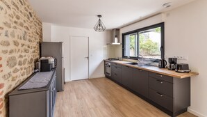 Moderni keittiö, jossa on kiviseinä, sisäänrakennettu uuni, pesuallas ja ikkuna, josta avautuu näkymä vehreään maisemaan.