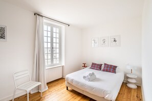 Une chambre à coucher comprenant un lit, une chaise, une fenêtre avec des rideaux et trois œuvres d’art accrochées au mur.