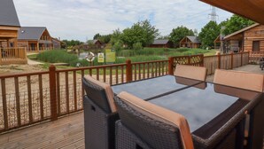 A wooden deck with a table and chairs, overlooking a pond and cabins. - Butterfly Lodge (Lincoln)