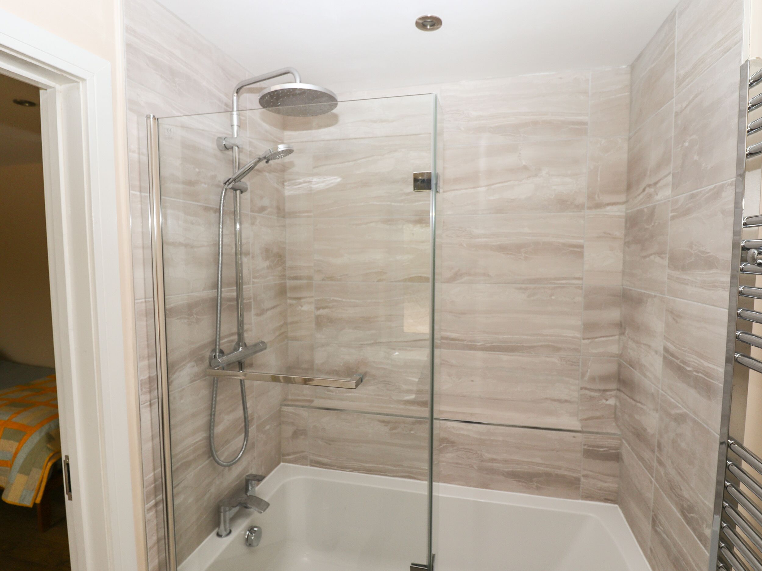 Eine Duschkabine mit Glaswänden, einer Handbrause und einem am Wand montierten Wasserhahn.