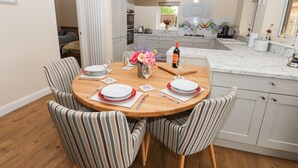 A dining area with a round table set for four, striped chairs, a vase of flowers, and a bottle of wine. - Butterfly Lodge (Lincoln)