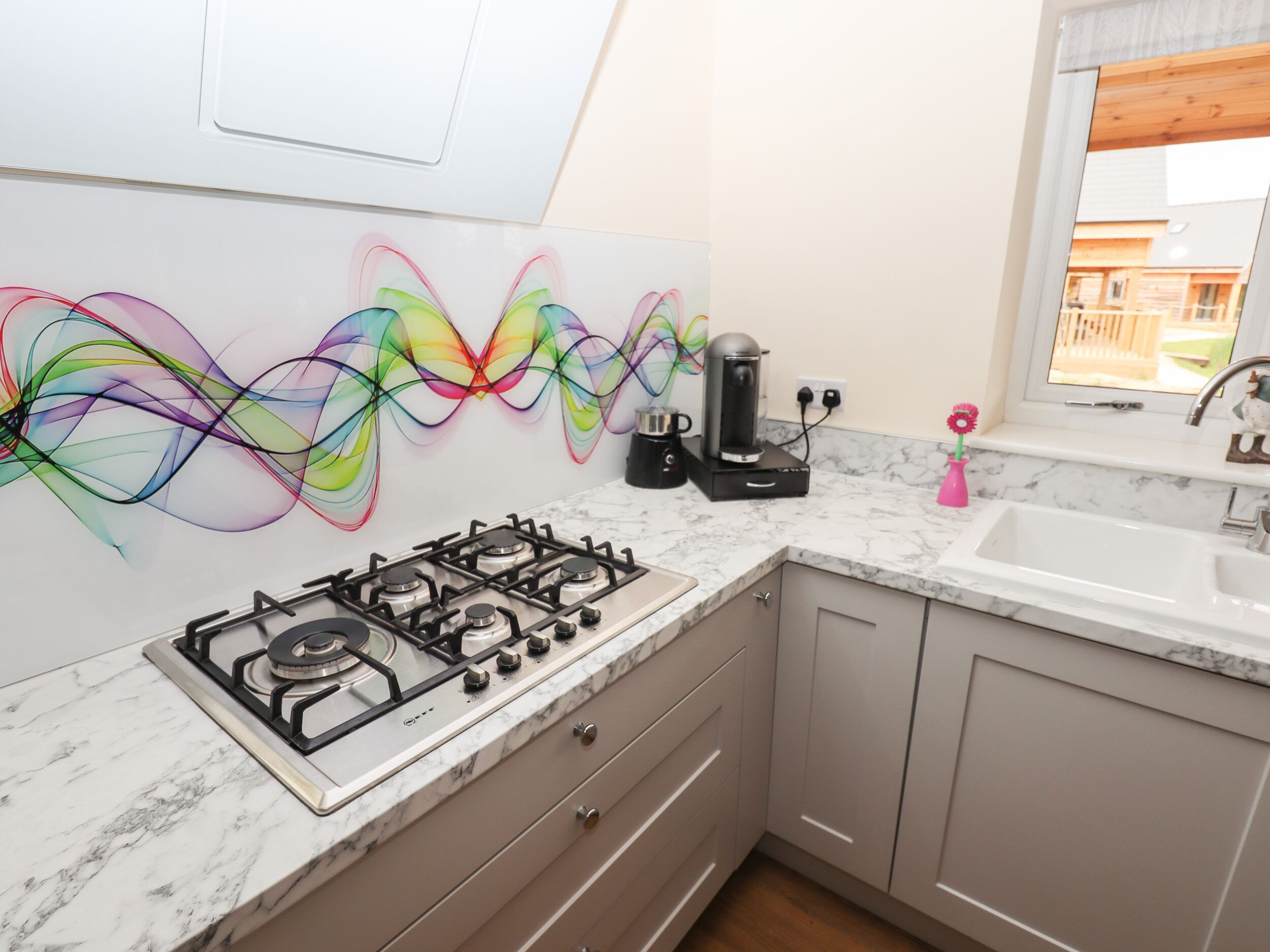 A modern kitchen with a gas stove, marble countertops, and a colorful abstract wall art.