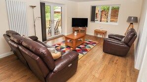 A living room with a brown leather sofa, a wooden coffee table, and a TV on a stand. There is a colorful rug on the floor. - Butterfly Lodge (Lincoln)
