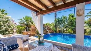 Un espacio al aire libre techado con piscina, muebles de mimbre y abundante vegetación.