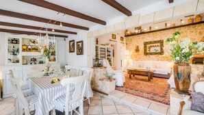 Amplia sala de estar con pared de piedra, un sofá blanco y un comedor con mantel a rayas.