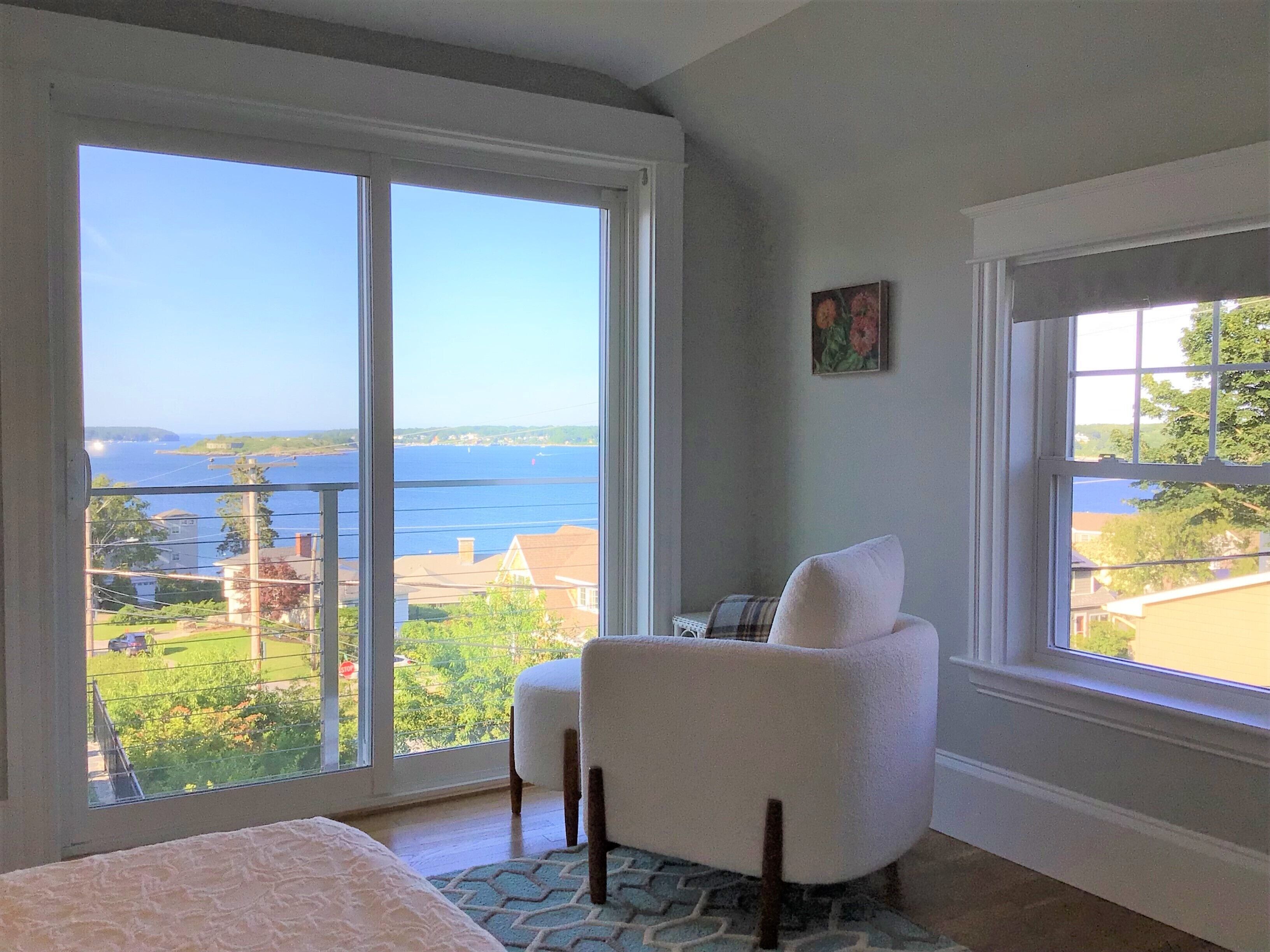 A bedroom with a large window offering a view of the sea and surrounding buildings.