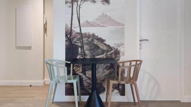 A dining area with a table and two chairs, a door with a painting, and a light switch on the wall. - Studio N#2 (Narbonne)