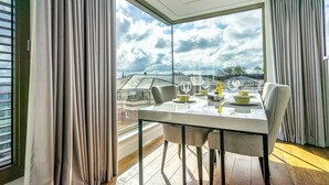 Un comedor moderno con un separador de vidrio, una mesa dispuesta con platos, vasos y cubiertos, y vistas al cielo y edificios.