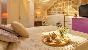 Een knus slaapkamer met een bed, een dienblad met thee en bloemen, een televisie en een stenen muur.