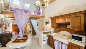Een ruime kamer met een hoge plafond, een wenteltrap, een eetgedeelte en een keuken met houten kastjes en een magnetron.