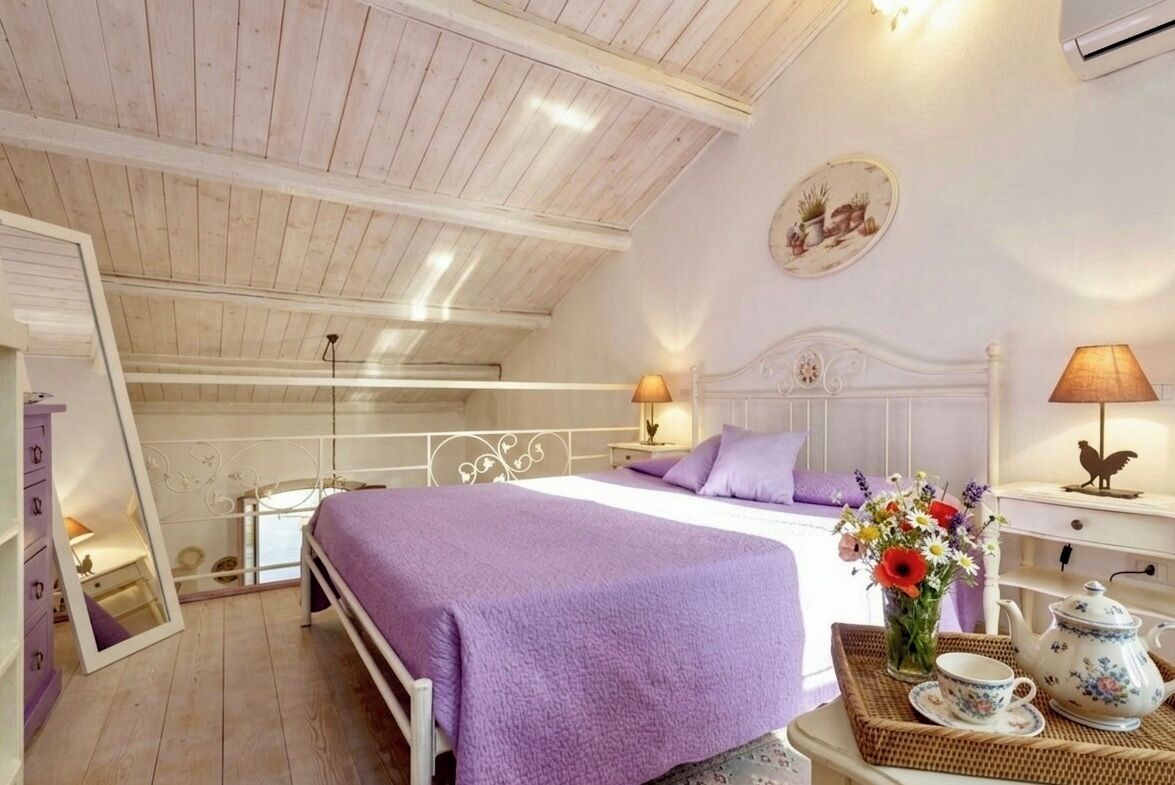 A bedroom with a bed, bedside tables, a mirror, a dresser, and a decorative vase with flowers.