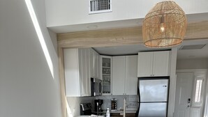 A modern kitchen with white cabinets, a stainless steel refrigerator, and a wooden dining table with stools.
