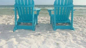 Two turquoise Adirondack chairs facing the ocean on a sandy beach.