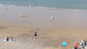 A beach with people engaging in various activities, a lifeguard tower, and a rocky shoreline. - The Plaice -  Wake up to panoramic sea views in The Plaice, Sheringham (Sheringham)