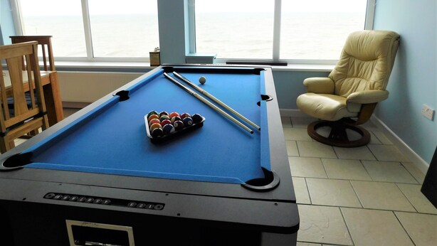 A pool table with balls and cues, a pool chair, and a window with a view of the sea. - The Plaice - Wake up to panoramic sea views in The Plaice, Sheringham (Sheringham)