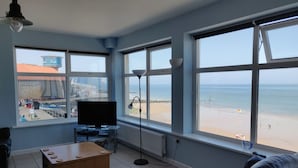 A living room with a large window overlooking a beach, a flat-screen TV, and a coffee table. - The Plaice -  Wake up to panoramic sea views in The Plaice, Sheringham (Sheringham)