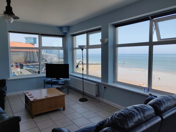 A living room with a large window overlooking a beach, a flat-screen TV, and a coffee table. - The Plaice - Wake up to panoramic sea views in The Plaice, Sheringham (Sheringham)