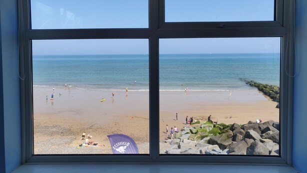 A beach view through a window with a clear sky, sandy beach, and rocky shoreline. - The Plaice -  Wake up to panoramic sea views in The Plaice, Sheringham (Sheringham)