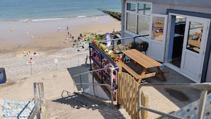 A beachside building with a staircase leading to a wooden deck with flowers and a table. - The Plaice -  Wake up to panoramic sea views in The Plaice, Sheringham (Sheringham)