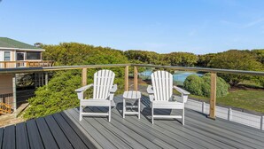 Eine Terrasse mit zwei Adirondack-Stühlen und einem kleinen Tisch, mit Blick auf einen Pool und üppiges Grün.