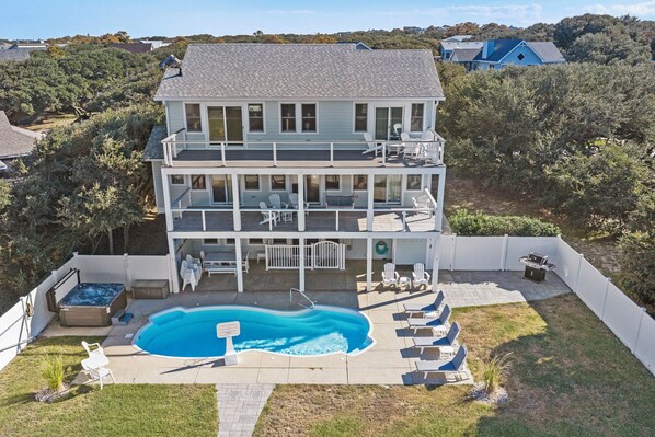 A two-story house with a swimming pool, outdoor seating, and a hot tub.