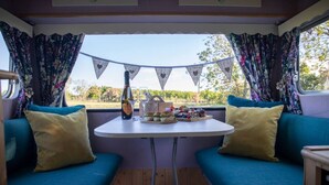 A cozy RV interior with a table set for a meal, featuring a bottle of wine, glasses, and a variety of snacks. - Private Glamping in a Vintage Caravan & Bell Tent (Morpeth)