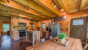 A rustic wooden interior with a kitchen featuring wooden cabinets, a stainless steel refrigerator, and a wooden dining table with a plant centerpiece. - Cozy Cabin, Great Location, Close to downtown, Private Hot Tub. (Gatlinburg)