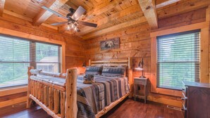 A wooden cabin bedroom with a bed, a nightstand, a ceiling fan, and a window with blinds. - Cozy Cabin, Great Location, Close to downtown, Private Hot Tub. (Gatlinburg)