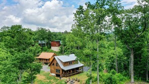 A wooden cabin with a porch and a fire pit, surrounded by dense forest. - Cozy Cabin, Great Location, Close to downtown, Private Hot Tub. (Gatlinburg)