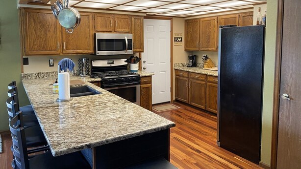 A kitchen with wooden cabinets, a stainless steel microwave, a black refrigerator, and a granite countertop. - Spacious 5 bedroom house minutes from Red Rocks (Littleton)