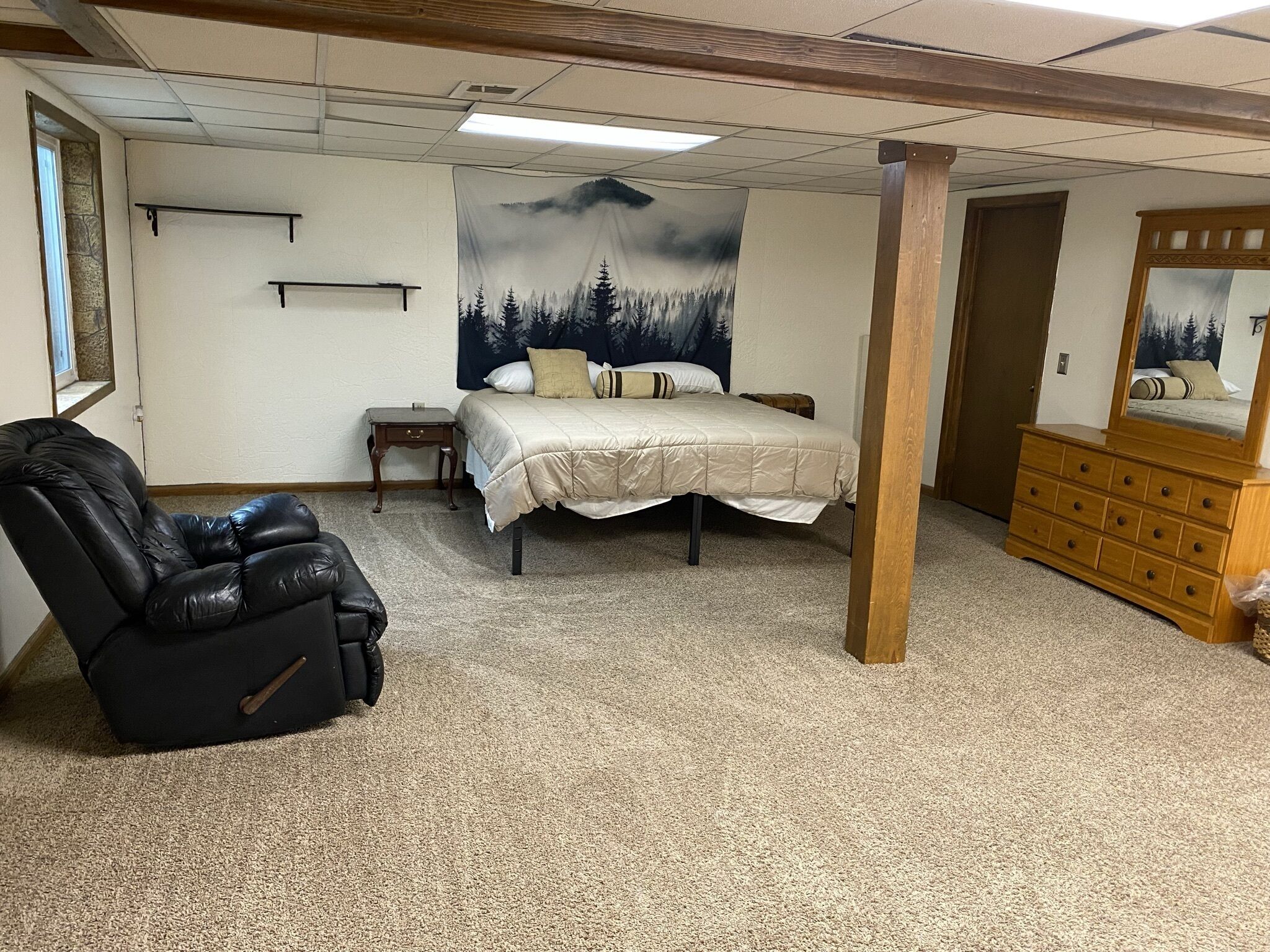 Un dormitorio con cama, una silla, cómoda y un tapiz en la pared.