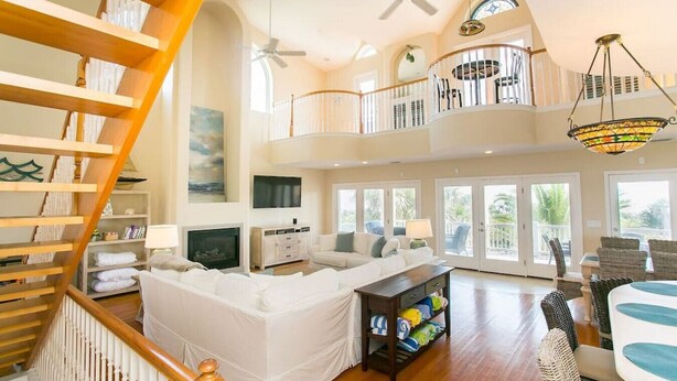 A spacious living area with a white sofa, a wooden staircase, and a balcony with a railing. - Luxury Oceanside Pool Home Boasting Incredible Views - Large 5/3 w/Heated Pool (St. Augustine)