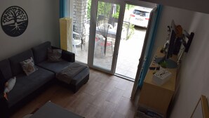 Un soggiorno con un divano grigio, un tavolino e una porta scorrevole in vetro che dà su una zona esterna con un'auto parcheggiata.