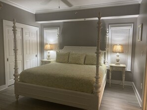 Una cama con dosel y tablero a juego, dos mesitas de noche con lámparas, y una puerta con tirador decorativo.